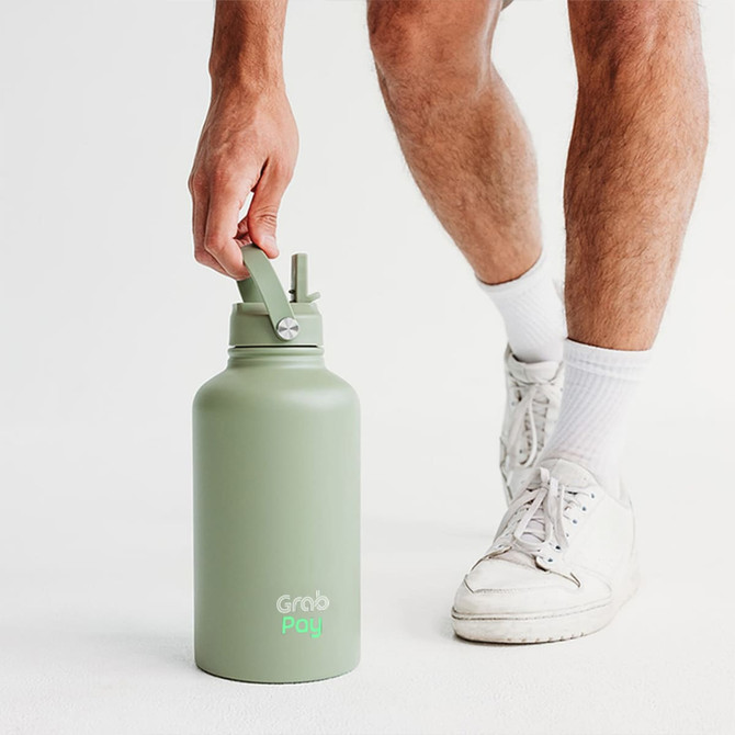 A drink bottle in matte green with a twist cap and straw, held by a person wearing white socks and sneakers.