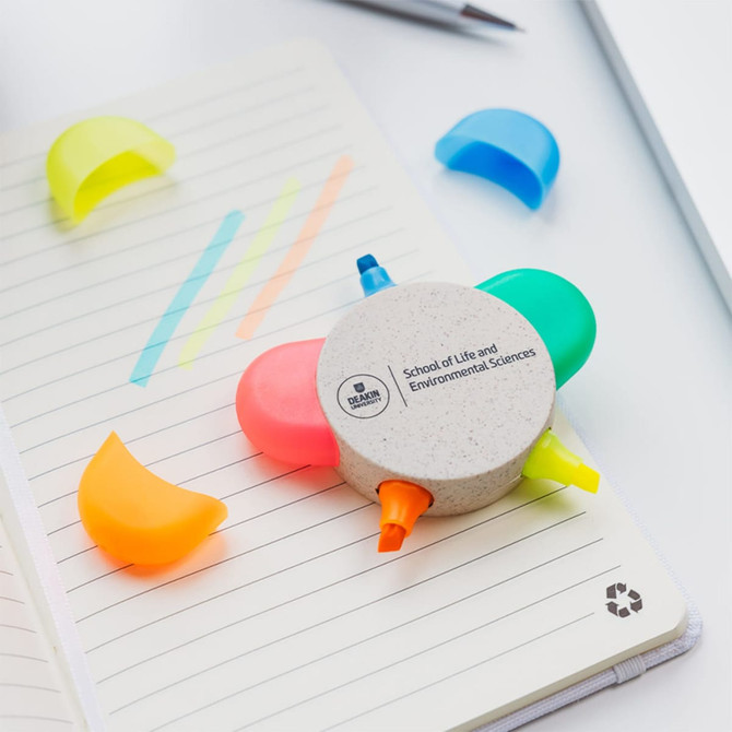 A set of eco-friendly highlighters in yellow, pink, green, and orange, arranged around a circular holder on a lined notebook.