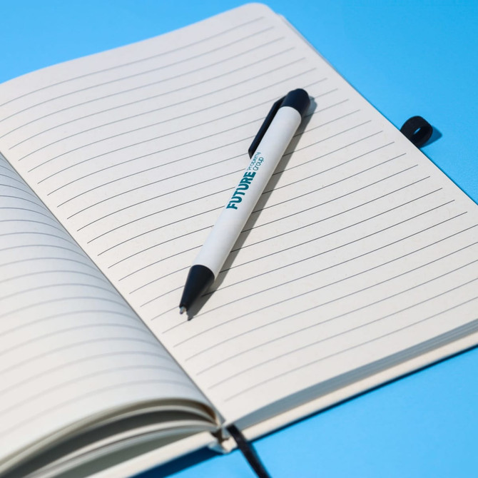 An A5 lined notebook in cream colour with a black pen resting on the pages, set against a blue background.