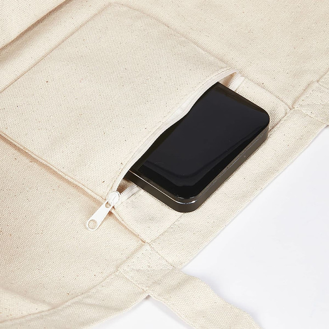 A large cream canvas tote bag with a black smartphone tucked into a zippered pocket.