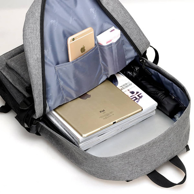 A grey laptop backpack with an open compartment displaying a laptop, magazines, and a mobile phone in pockets.