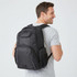 A black laptop backpack with multiple compartments, worn on the back of a person smiling. It features a logo.