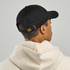 A black organic dad hat with an adjustable strap, worn backward by a person in a light-coloured hoodie.