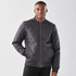 A man wearing a charcoal grey thermal jacket with a quilted design and a front zip closure. The jacket has a branding logo.