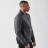 A men's thermal jacket in dark grey, featuring a quilted design and ribbed cuffs. The model stands in profile.