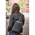 A sleek black and grey sling backpack is worn across the back of a person in a city setting.