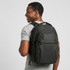 A man wearing a black Exton laptop backpack, featuring multiple compartments and a logo.
