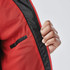 A close-up of a red jacket with a black lining, featuring a hand holding the zipper area. The jacket has a logo.