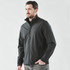 A man wearing a black softshell jacket with a zipped front and high collar, featuring a logo.