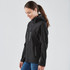 A woman wearing a black softshell jacket with a hood, featuring zippered pockets and a fitted design.