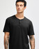 A black unisex Henley T-shirt featuring short sleeves and a button-up neck. The model has tattoos on their arms.