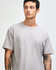 A grey American Apparel Super Heavyweight T-Shirt displayed on a model with curly hair. The shirt has a logo.