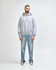 A grey hooded sweatshirt is worn by a male model, paired with black jeans and sneakers. The sweatshirt has a logo.