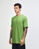 A green unisex short sleeve t-shirt displayed on a model from the side, featuring a branding logo.