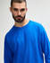 A blue long sleeve t-shirt worn by a model, featuring a relaxed fit and branding on the sleeve.