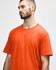 An orange Gildan Softstyle adult midweight t-shirt worn by a model. The shirt has a round neckline and short sleeves.