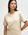 A midweight adult T-shirt in a neutral beige colour, displayed on a model with a casual pose. The shirt features a logo.