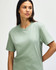 A model wearing a midweight T-shirt in a soft green colour. The T-shirt has a simple design and features a logo.