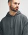 A soft grey hooded sweatshirt, featuring a front pocket and a hood, worn by a model. It has a small logo.