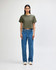 A woman stands wearing an olive green boxy t-shirt and light blue cargo jeans, paired with black and white sneakers.