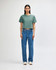 A model wears a green boxy t-shirt with light blue cargo jeans and sneakers, featuring a casual style.