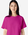 A woman wearing a bright pink boxy t-shirt, featuring a crew neck and short sleeves. The shirt has a logo.