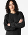 A black long sleeve t-shirt displayed on a model with curly hair, featuring a logo on the garment.