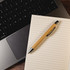A bamboo stylus pen rests atop a blank notepad, next to a laptop keyboard.