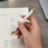 A gold and white metal pen is held above a document with detailed financial statements.