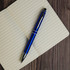 A blue aluminium pen with silver accents rests on an open lined notebook.