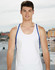 A model wearing a plain white tank top with blue straps, standing by a waterfront. The background features a dock and buildings.