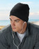 Acrylic knitted marl beanie in dark grey worn by a model with earbuds, set against a coastal background.