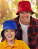 A red bucket hat and a blue bucket hat worn by a man and a girl, both smiling. The background is blurred greenery.