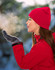 A woman in a bright red beanie and gloves exhales visibly in a snowy outdoor setting.