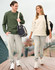 A unisex crew neck sweater in olive green and cream, paired with grey pants, worn by a man and woman walking outdoors.