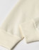 A crew neck sweater in a creamy off-white colour, featuring ribbed cuffs and a smooth fabric texture.
