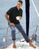 Men's flexi chino pants in navy, modelled by a man on a boat, wearing a black polo and holding a cup.