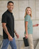 A black men's polo and a green women's polo are worn by two people against a neutral background. Both garments have logos.