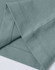A close-up of a light green premium cotton T-shirt, highlighting the sleeve and stitching details. The shirt has a logo.