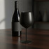A black stainless steel wine glass stands beside a wine bottle on a wooden table. The setting has soft, ambient lighting.