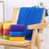 A stack of vibrant gym towels in purple, pink, blue, and orange, placed on a wooden chair with a larger blue towel draped on the back.