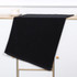 A black gym towel laid flat on a light wooden surface, featuring a clean design with a simple border.