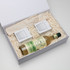 A drink bottle with a light green label and two small boxes inside a white gift box filled with shredded paper.