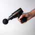 A black massage gun with a spherical attachment, held in a hand, featuring a sleek design and gold accents.
