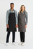 A black and a grey bib apron are displayed on two models, with each wearing a collared shirt and pants.