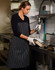 A black and white striped apron worn by a woman in a kitchen, featuring a logo, while washing dishes.