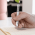 A metal pen with a silver body is held above lined paper, featuring a logo on its side.