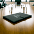 A black portfolio with a logo, resting on a wooden conference table, surrounded by glasses of water.