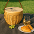 A wicker cooler basket in natural tones, with a wooden lid, alongside a glass of white wine, grapes, and croissants.