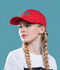 A red cotton twill cap with a buckle, featuring a logo, worn by a model with braided hair against a blue background.